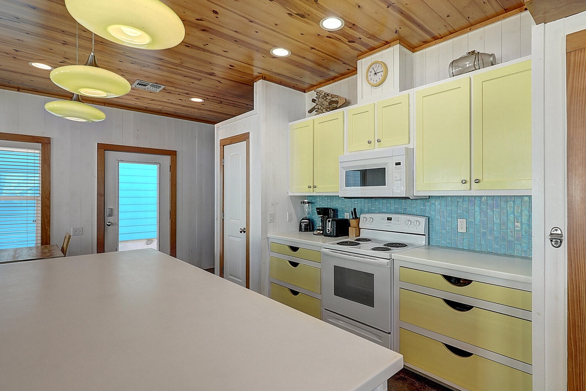 Your bright, cheerful kitchen awaits with sunny yellow cabinets and turquoise tile backsplash, perfect for whipping up coastal-inspired meals.