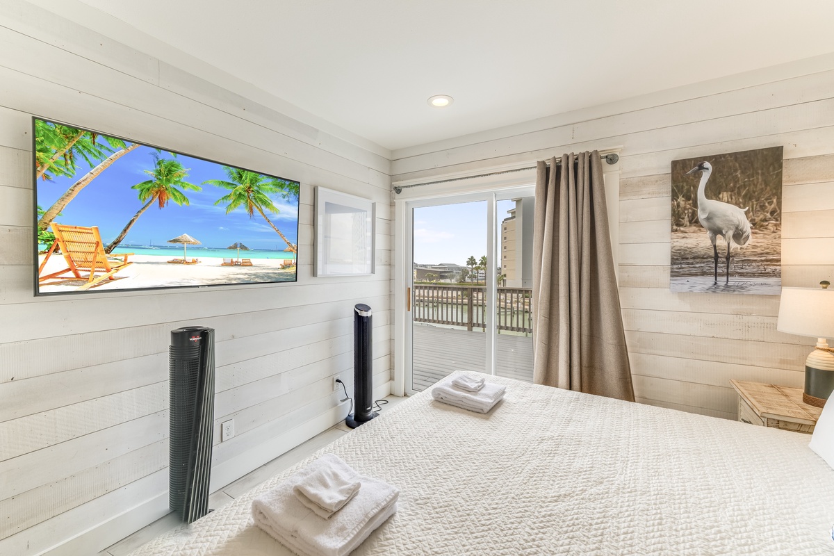 Your serene bedroom retreat opens to a spacious balcony with views of the surrounding area. Crisp white linens await, perfectly folded towels rest ready, and coastal artwork adds character to this peaceful space.
