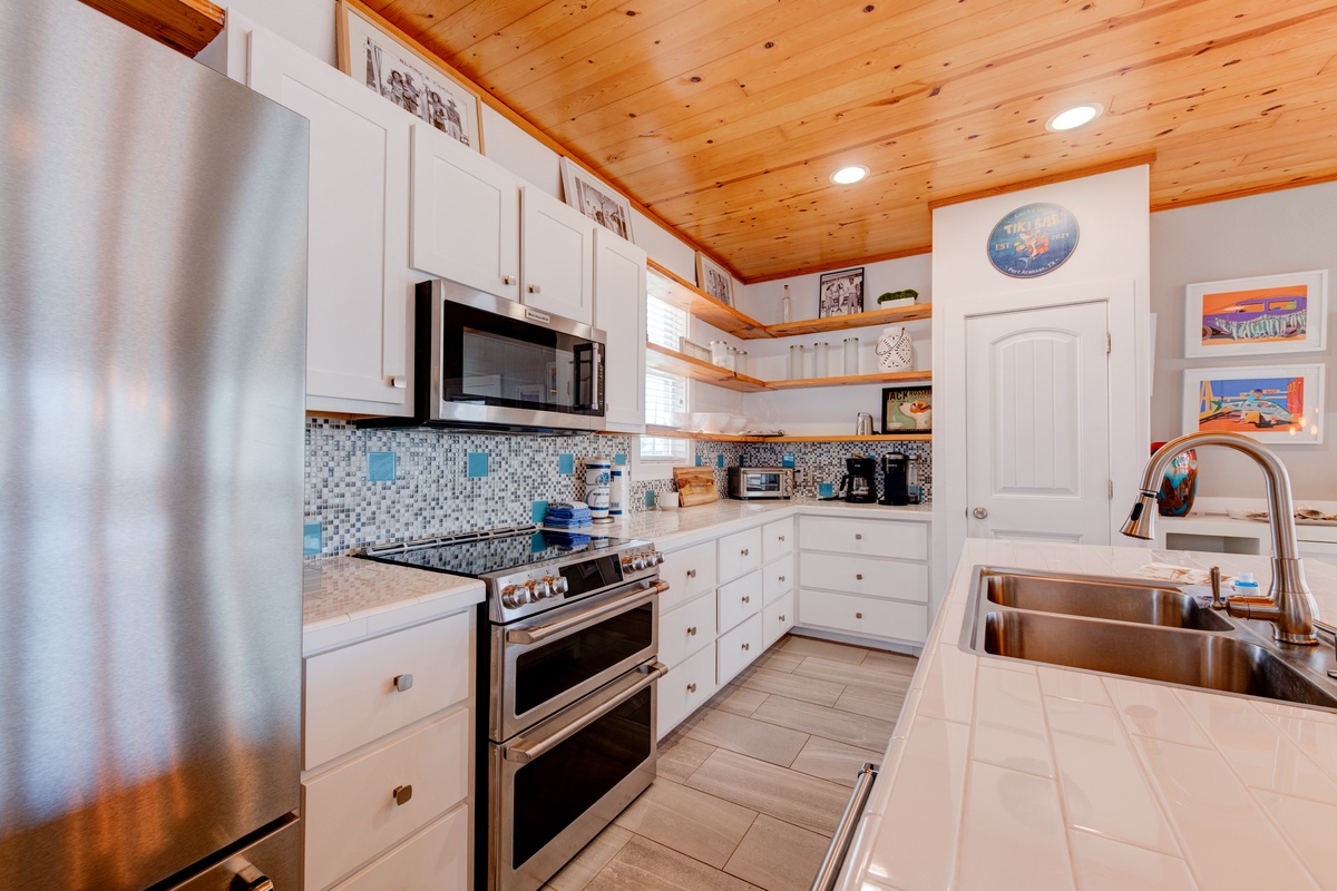 Your fully equipped kitchen awaits with stainless steel appliances, granite countertops, and charming coastal touches under warm wood ceilings.