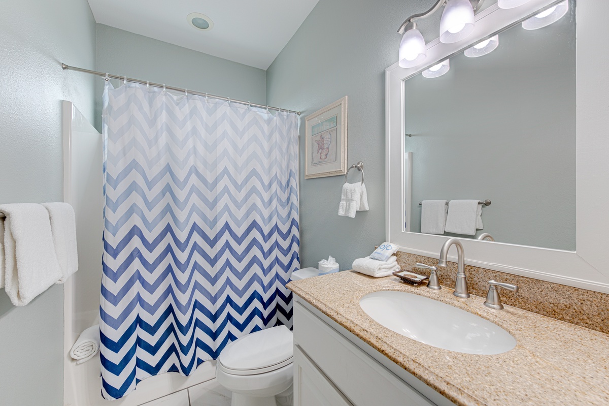 Step into your spa-inspired bathroom featuring a stylish chevron shower curtain and granite vanity, perfectly lit for your daily routine.