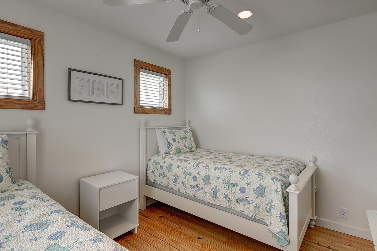 Rest peacefully in your bright twin bedroom featuring charming coastal bedding, warm wood floors, and gentle ceiling fan comfort.