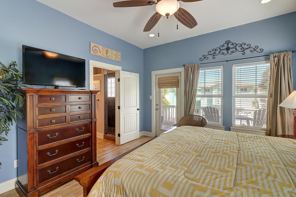Relax in your peaceful blue bedroom with comfortable furnishings, ceiling fan, flat-screen TV, and charming balcony access for morning coffee.