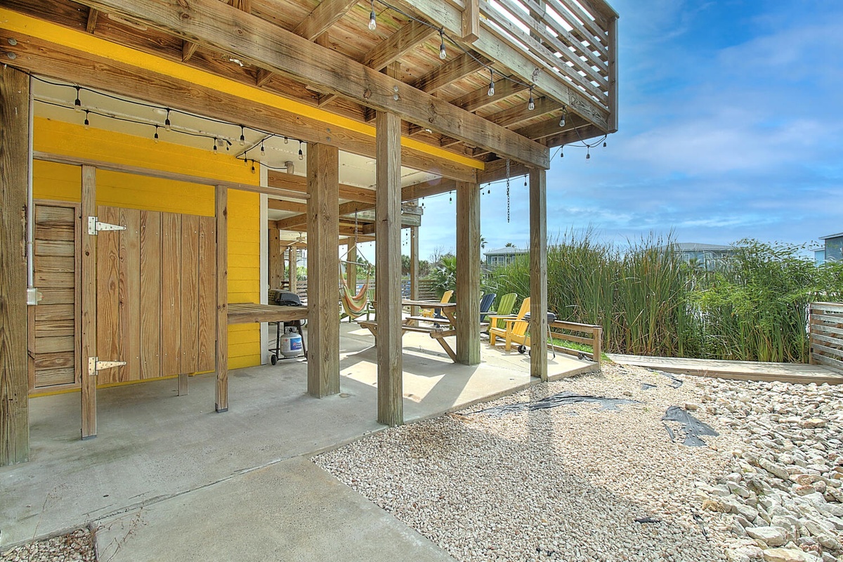 Your private covered patio awaits with yellow Adirondack chairs and string lights, perfect for sunset cocktails overlooking the coastal landscape.
