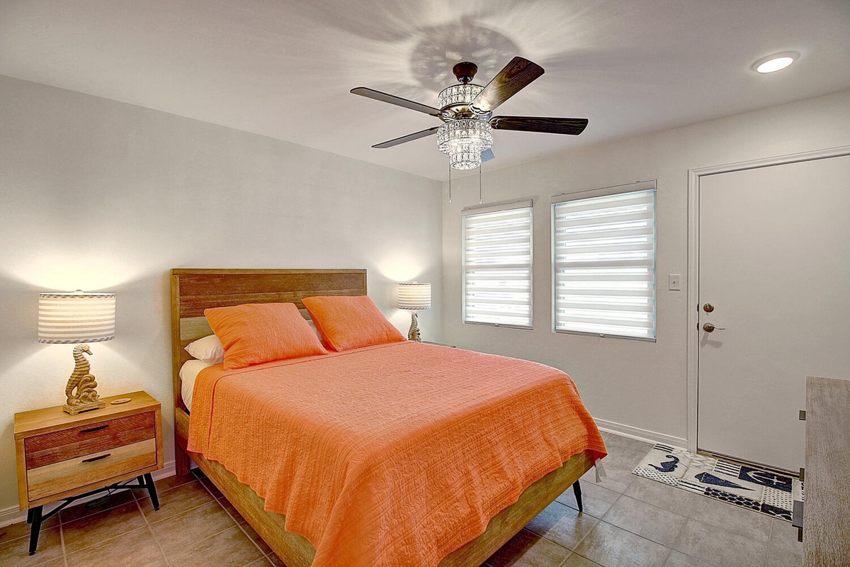 Rest comfortably in your stylish bedroom featuring vibrant orange bedding, elegant crystal ceiling fan, and warm bedside lighting for perfect relaxation.