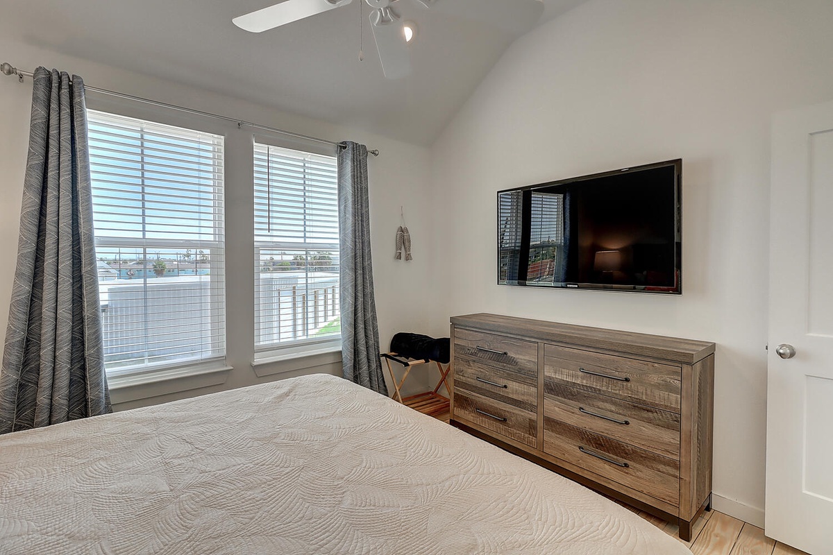Unwind in your bright bedroom with rustic wood furnishings, wall-mounted TV, and natural light streaming through stylish curtains.