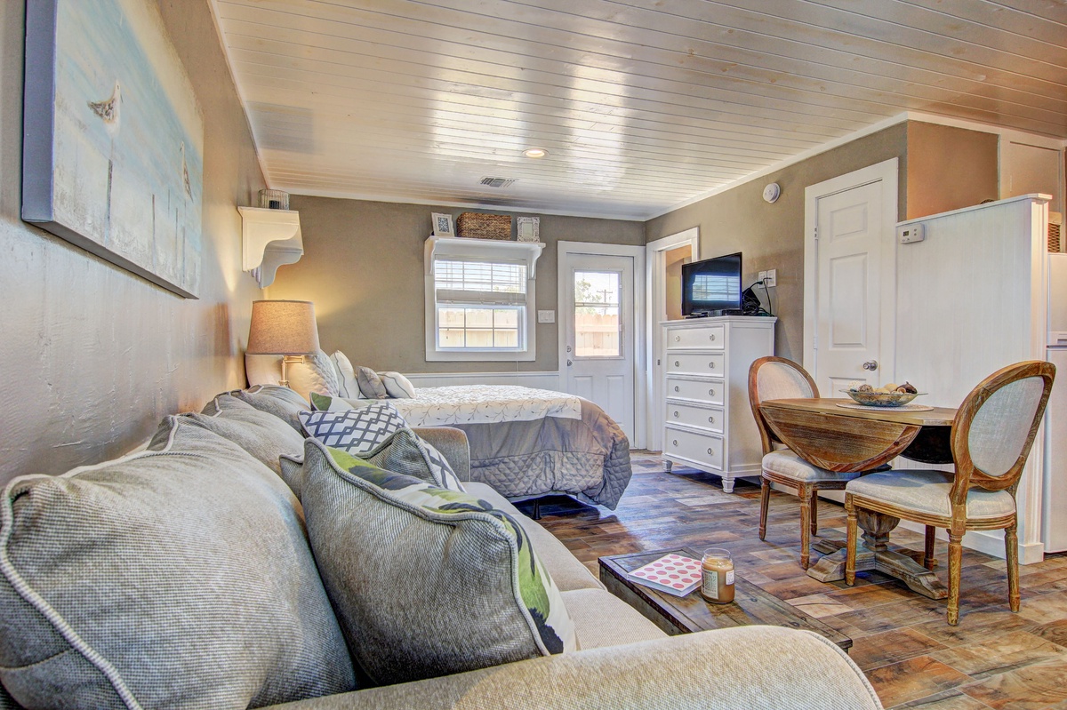 Your charming studio features a cozy sofa and peaceful sleeping area with elegant furnishings and natural light streaming through windows.