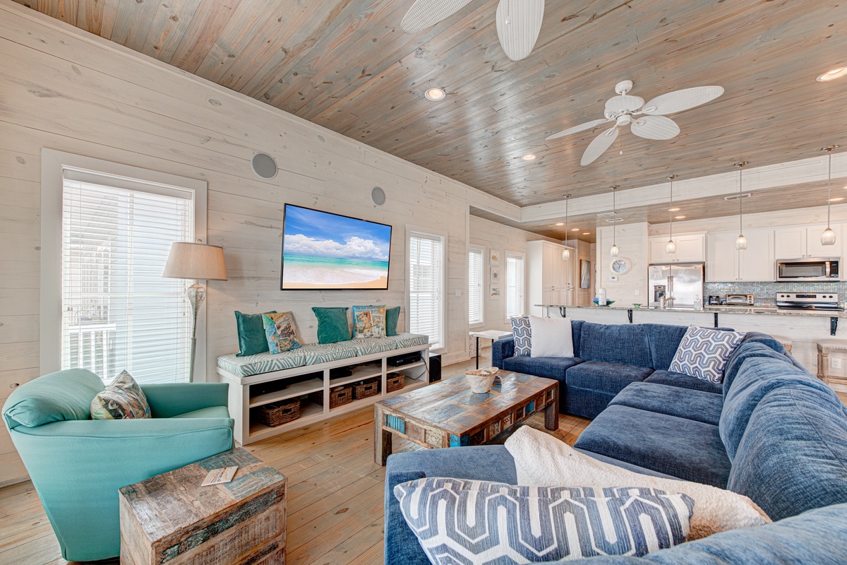 Relax in this coastal living space with plush seating, wood ceilings, and open kitchen where comfort meets beach vibes.