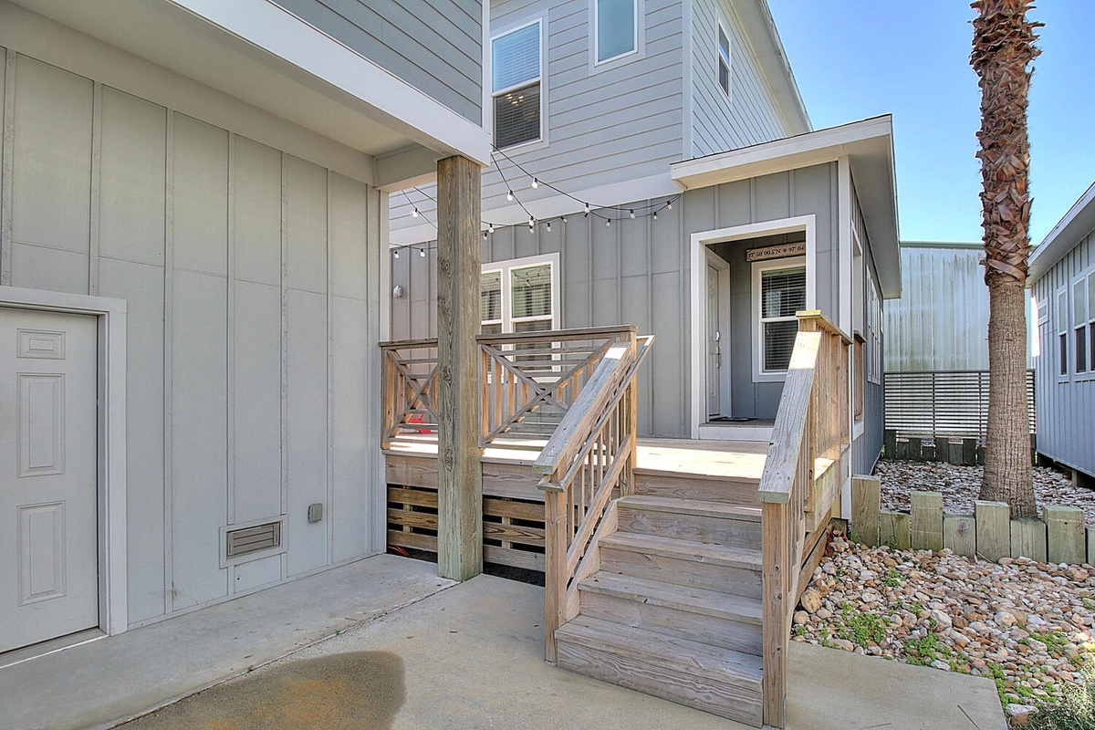 Modern coastal property featuring elevated deck entry with wooden stairs and tropical palm tree accents.