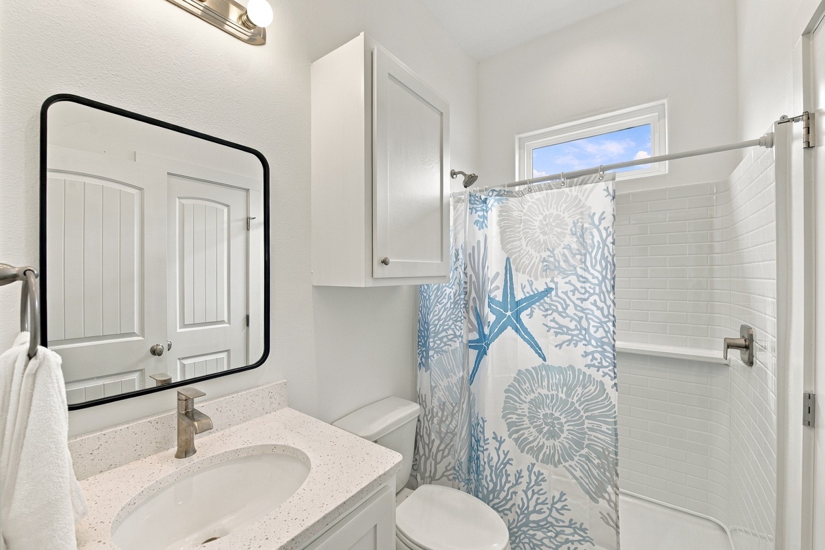 Primary coastal-inspired bathroom with a walk-in shower, crisp white cabinetry, a beach-themed shower curtain, and subway tile that sets a fresh, relaxing tone for your mornings.