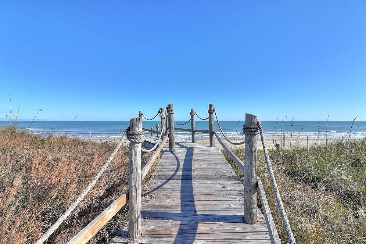 Scenic beach access with wooden boardwalk leading to pristine sandy shores and ocean views.