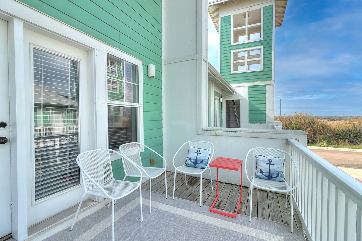Relax on your private deck with nautical touches, white metal seating, and open coastal views stretching beyond.