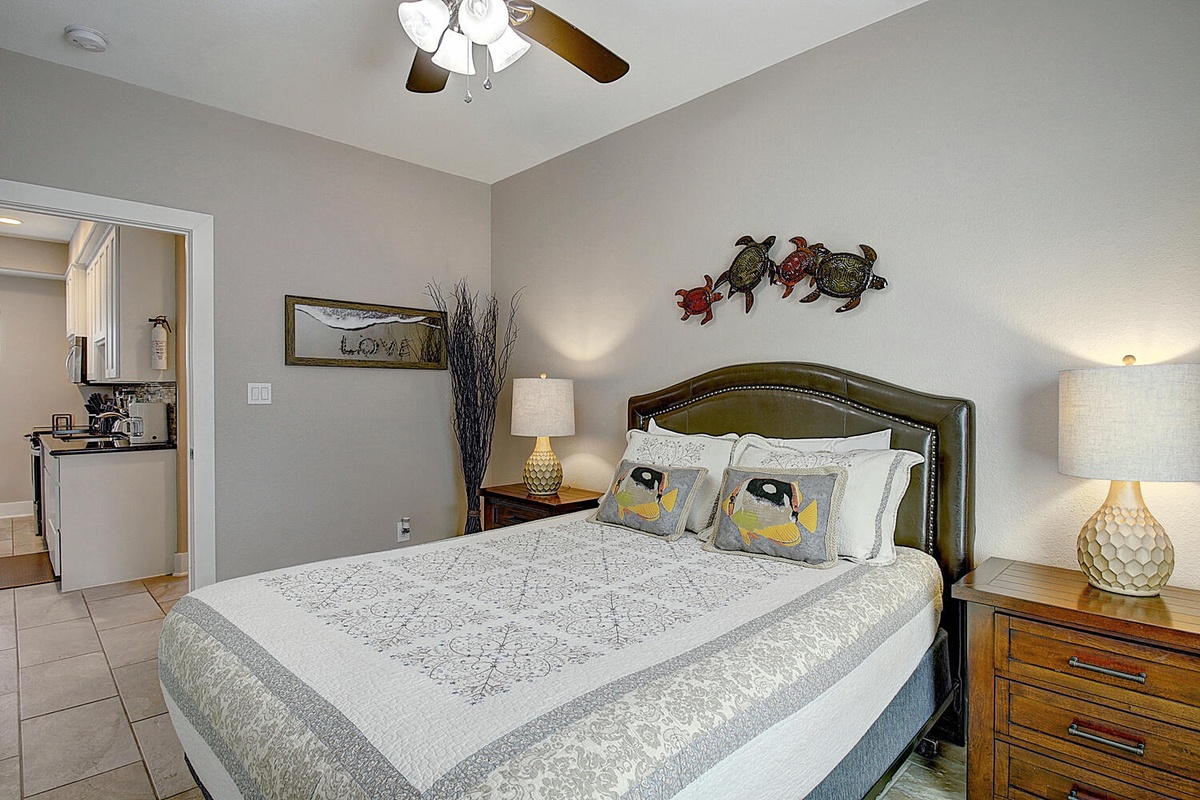 Drift off in your comfortable king bed beneath the gentle ceiling fan, with charming coastal touches and warm lighting creating perfect ambiance.