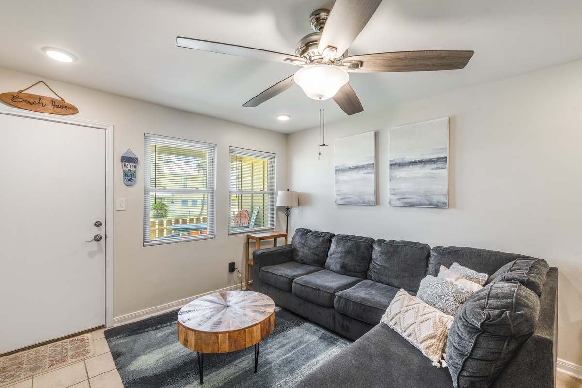 Sink into your comfortable sectional sofa and feel the gentle breeze from your ceiling fan in this bright, coastal-themed living space.