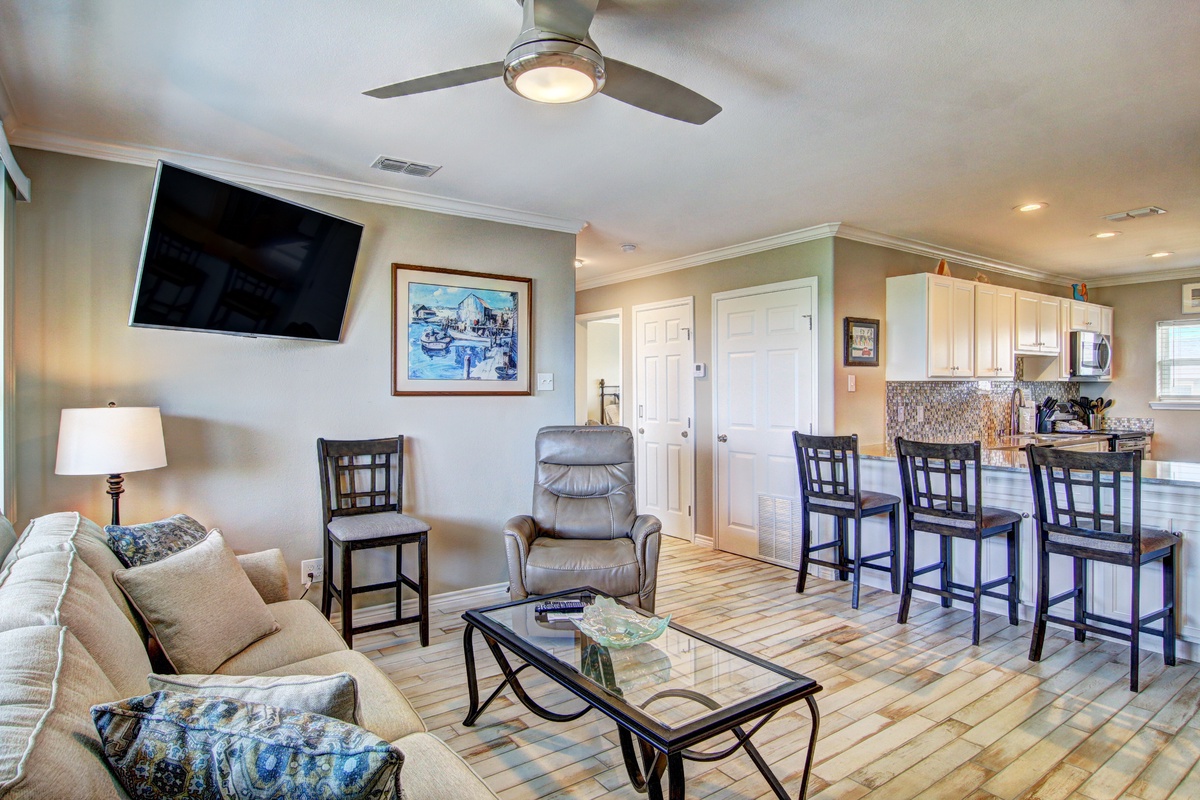Relax in your open-plan living space featuring a plush sofa, entertainment center, and breakfast bar that flows seamlessly into the kitchen.