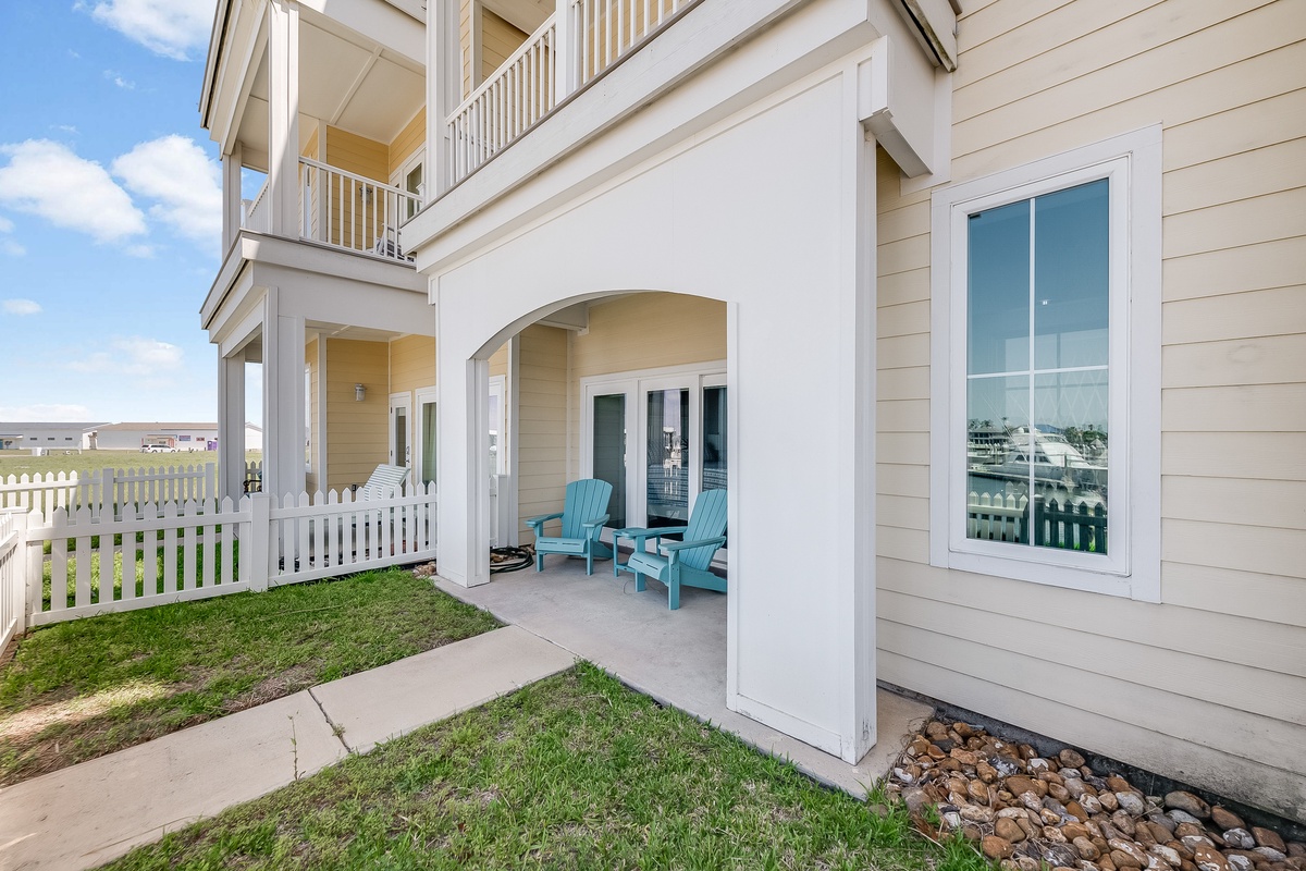 A charming coastal-style building exterior featuring multiple balconies and a covered patio area with blue chairs.