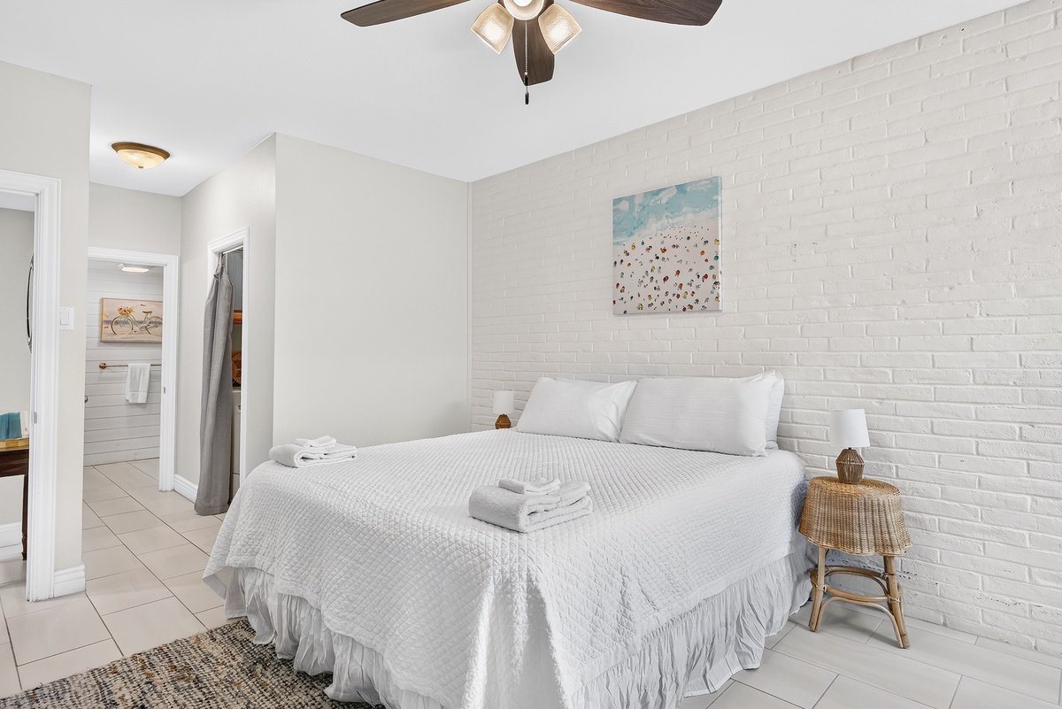 Unwind in your serene bedroom with crisp white linens, coastal charm, and a ceiling fan to keep you cool after your beach day.