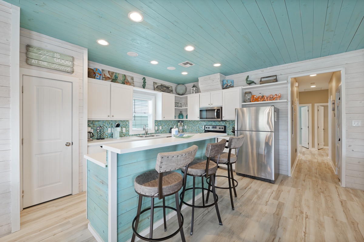 Picture yourself cooking meals in this coastal-inspired kitchen, where turquoise accents and beach décor create a breezy, relaxed atmosphere. Gather at the island on comfy stools and enjoy the bright, open layout.