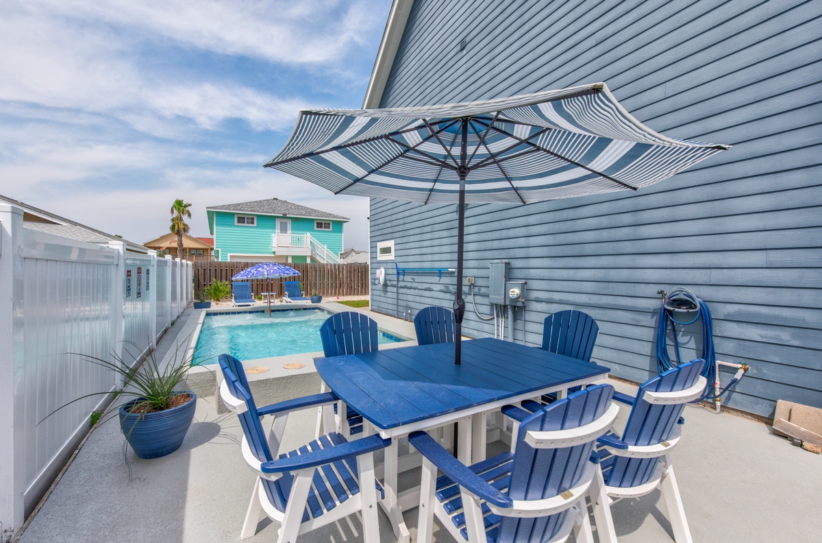 Your private patio offers poolside dining with vibrant blue chairs and striped umbrella shade, perfect for sunny meals and refreshing dips.