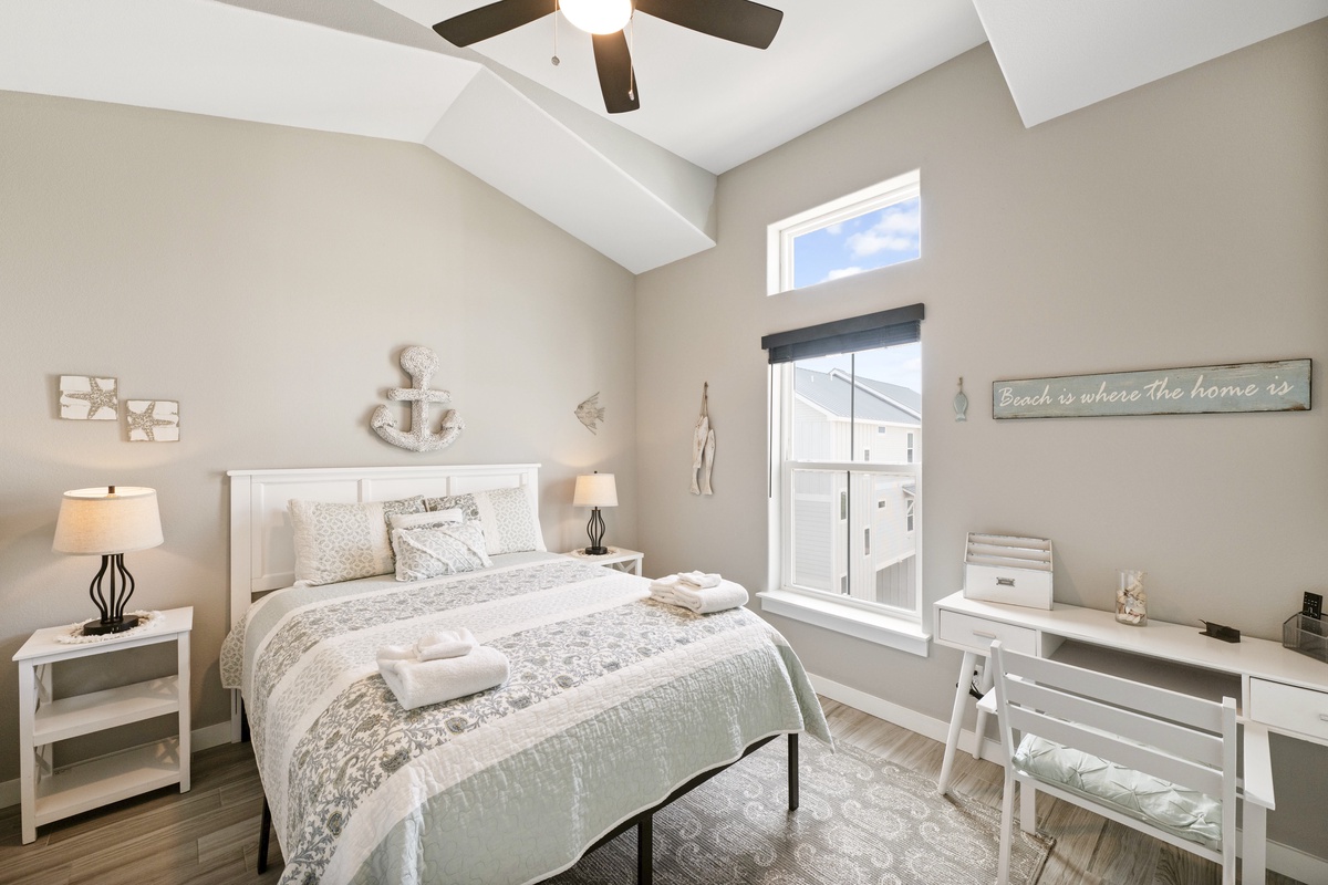 Drift off in this serene coastal-themed bedroom with soft linens, nautical touches, and ceiling fan for perfect comfort.