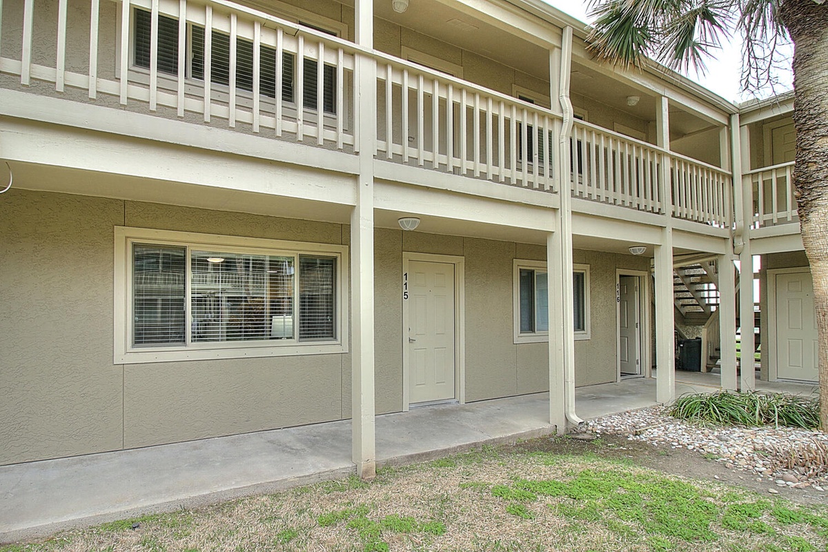 Two-story building exterior featuring ground-floor accommodations with covered patios and upper-level balconies with white railings.
