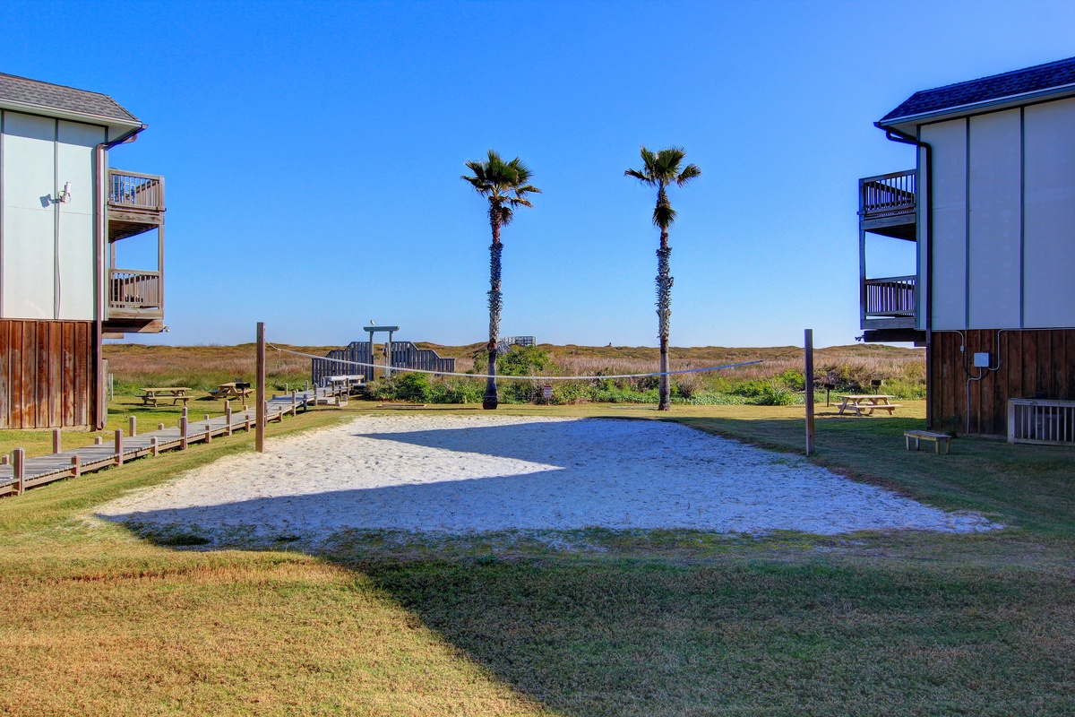Modern beachside buildings with palm trees and coastal boardwalk access to nearby dunes and shoreline.