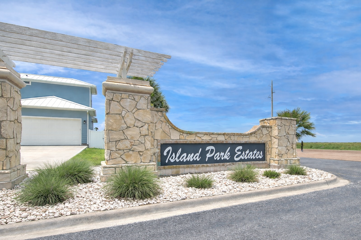 Elegant stone entrance to Island Park Estates features modern architecture and professional landscaping under clear blue skies.