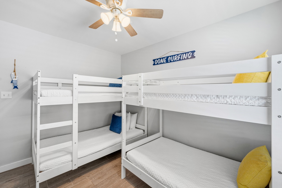 Sleep soundly in this cheerful bunk room with crisp linens and playful beach vibes. The ceiling fan keeps things cool while the 'Gone Surfing' sign adds coastal charm perfect for young adventurers.