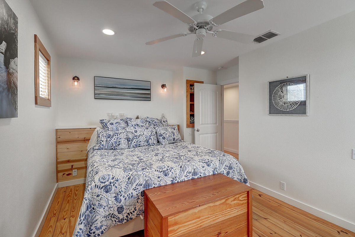 Drift off in this cozy bedroom featuring handcrafted wood details, peaceful coastal artwork, and a gentle ceiling fan for perfect climate comfort.