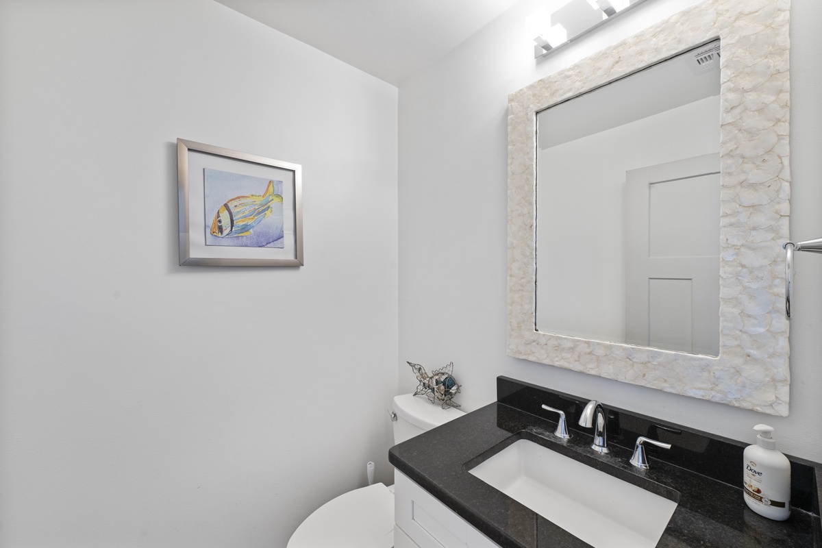Refresh in your elegant bathroom featuring a shell-framed mirror, granite countertops, and charming coastal artwork.