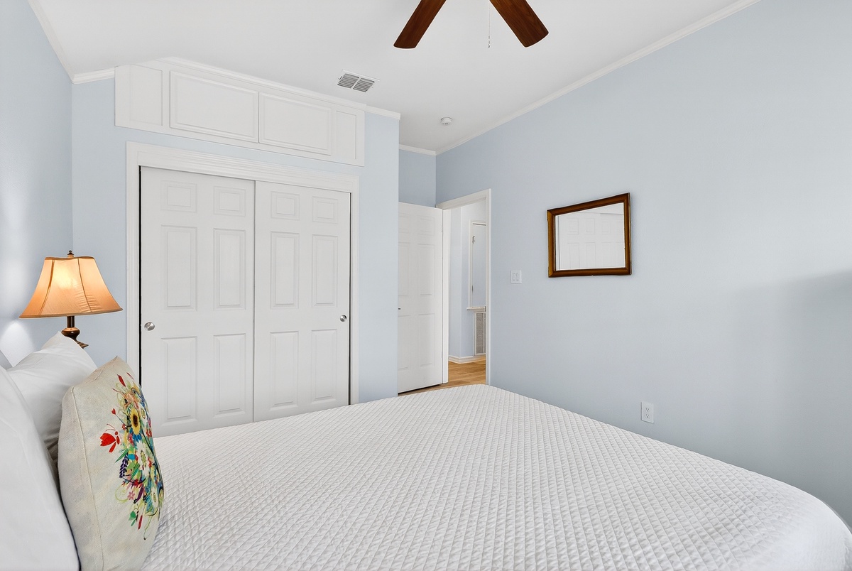 Drift off in this serene bedroom with soft blue walls and cozy linens, where your ceiling fan keeps you cool.