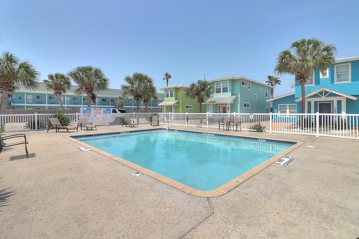 Community pool surrounded by colorful beach houses and palm trees creates a tropical resort atmosphere.
