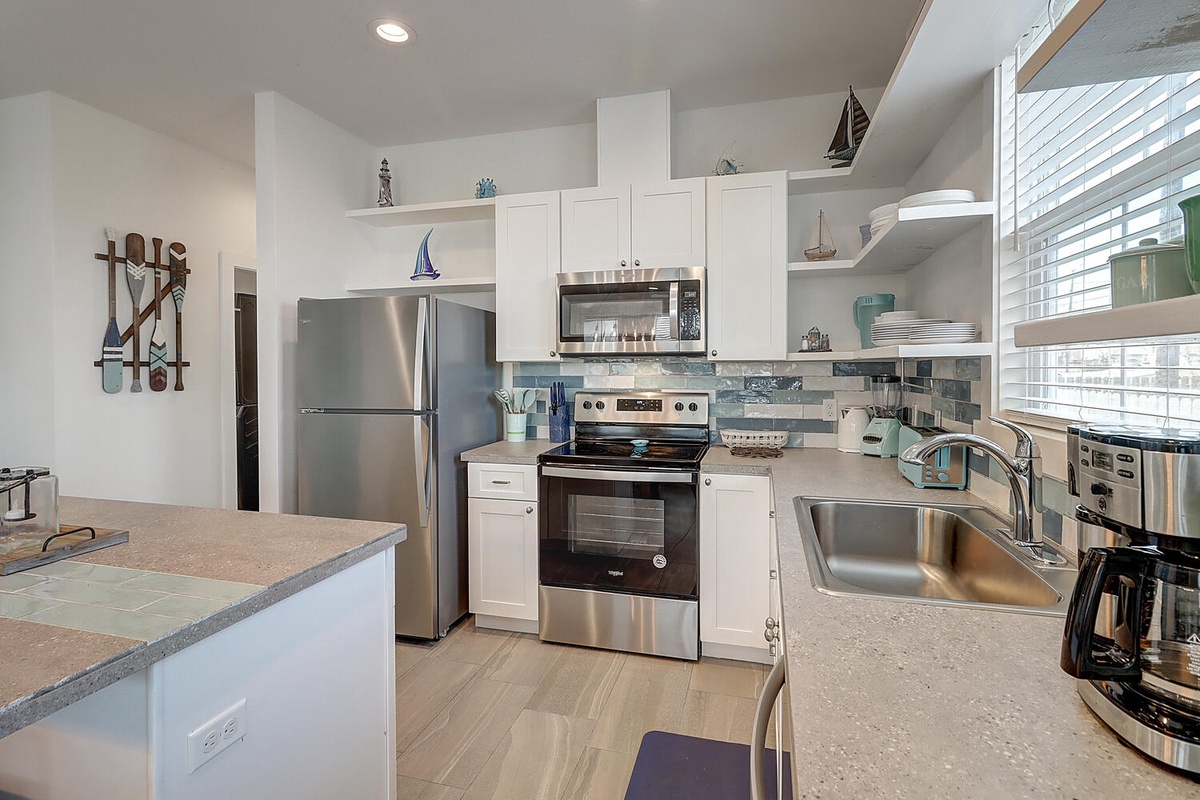 Your fully equipped kitchen features granite countertops, stainless steel appliances, and coastal decor perfect for preparing vacation meals together.