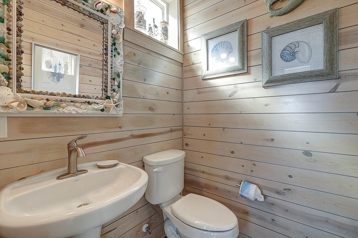 Your private powder room combines coastal charm with rustic wood paneling, featuring seashell-framed mirrors and nautical art that make freshening up feel like a seaside escape.