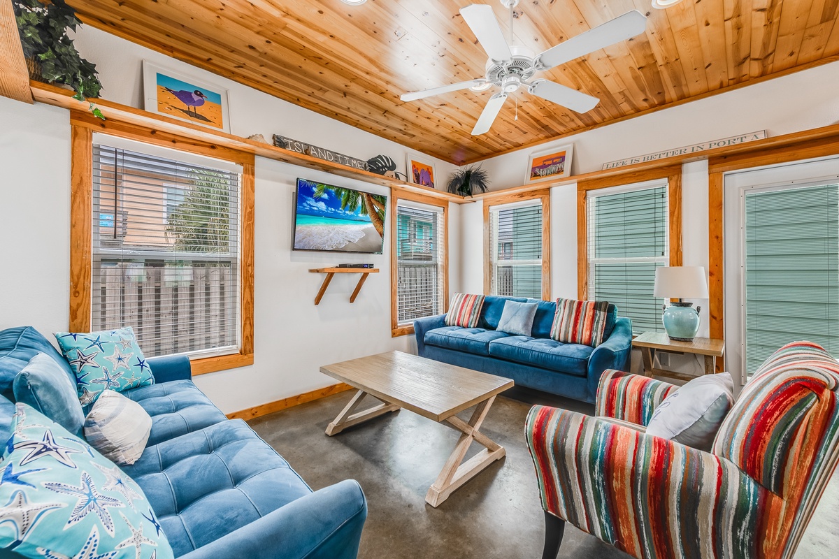 Unwind in your cozy living room featuring plush blue sofas, warm wood ceilings, and colorful coastal decor that creates the perfect beach retreat atmosphere.