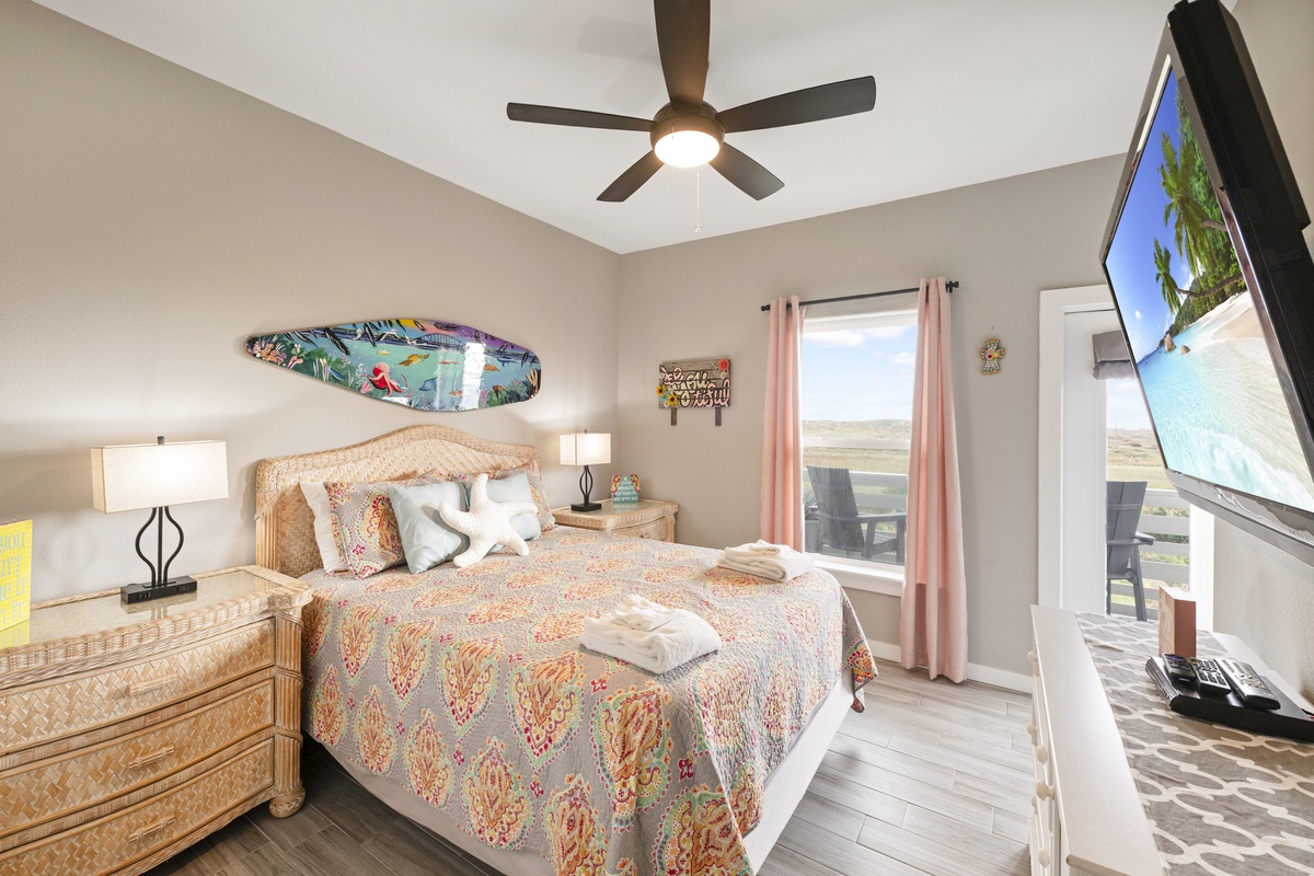 Drift off to coastal dreams in your bright bedroom with tropical surf decor, ceiling fan comfort, and wall-mounted TV for relaxing evenings.