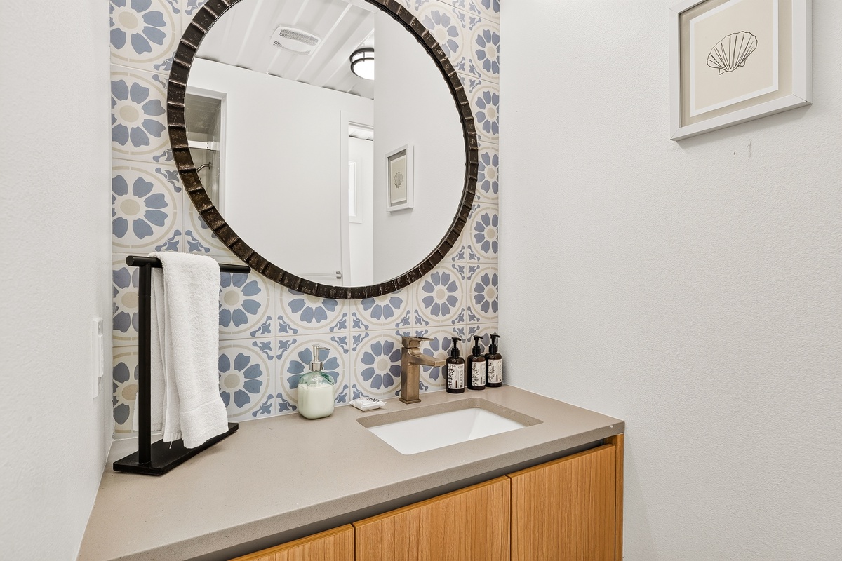A coastal-inspired guest bathroom welcomes you with charming Spanish tile and a statement round mirror, creating a fresh, airy retreat for your daily routine.