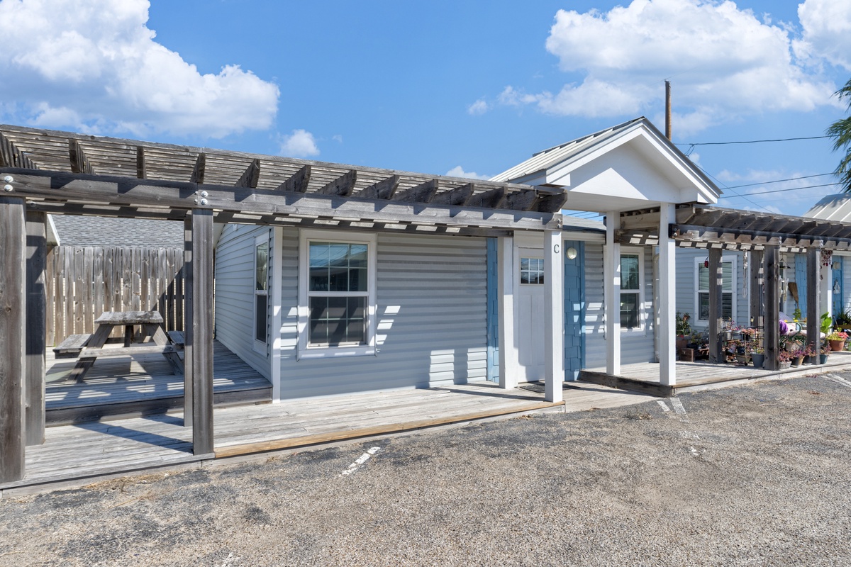 Charming coastal cottage with covered porch and outdoor seating areas under sunny blue skies.