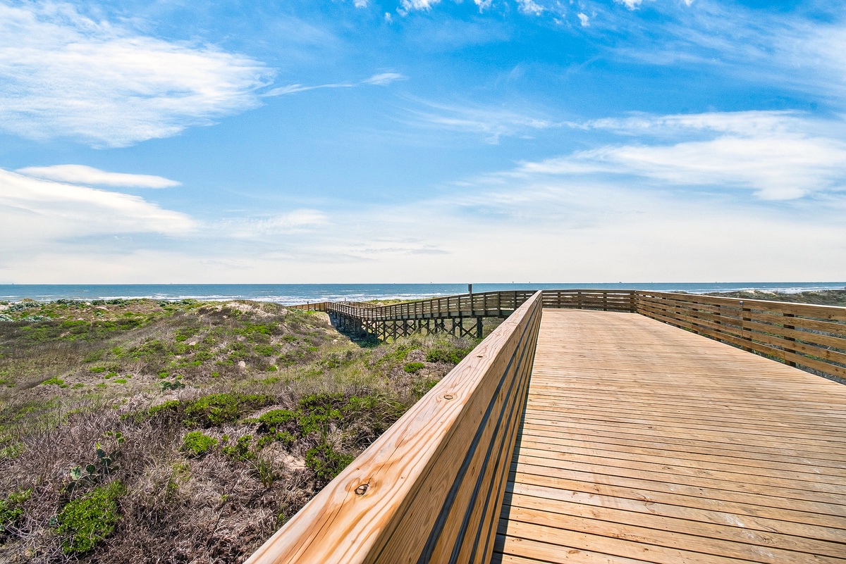 Wooden boardwalk winds through coastal dunes toward the ocean, offering peaceful pathways to the beach.