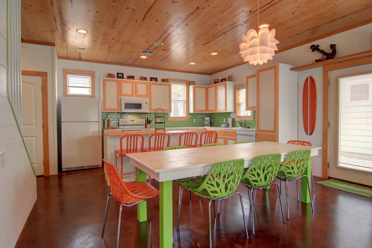 Your bright, beachy kitchen and dining space features vibrant orange cabinets, green subway tiles, and colorful chairs perfect for memorable meals together.