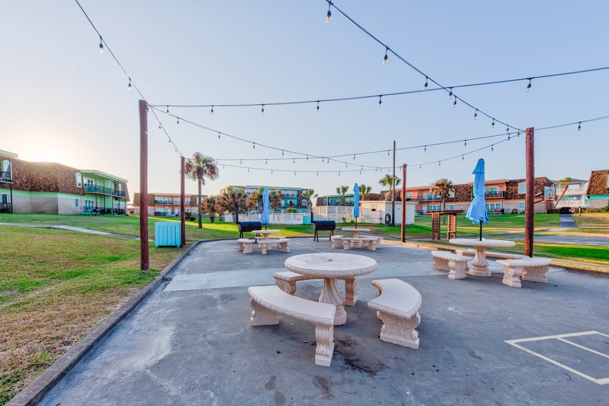 Outdoor picnic pavilion with string lights creates a perfect gathering spot among colorful resort buildings and landscaped grounds.