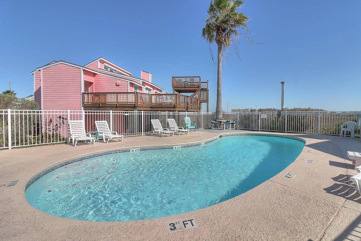 A charming pink coastal property featuring a private kidney-shaped pool, spacious deck with lounge chairs, and multi-level balconies overlooking the water. Perfect for sunny days and relaxing poolside.