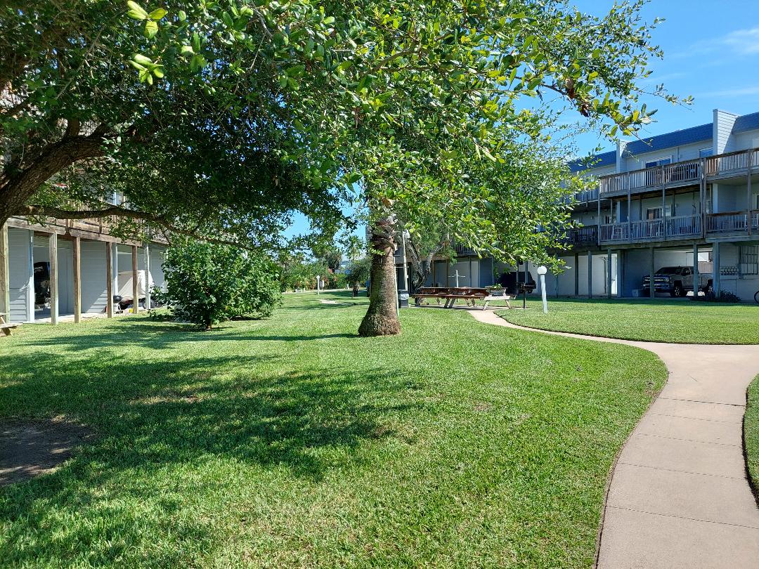 The property features spacious green lawns and mature trees creating a peaceful courtyard setting.