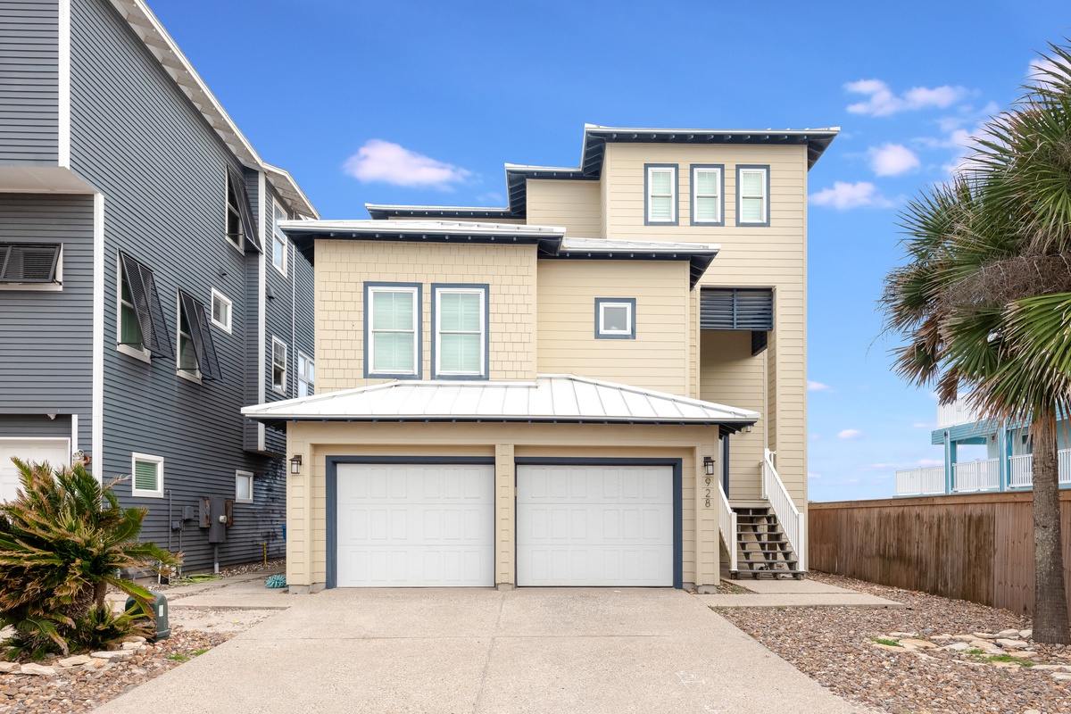 Modern three-story coastal home with tropical landscaping and convenient two-car garage in a charming beach community.