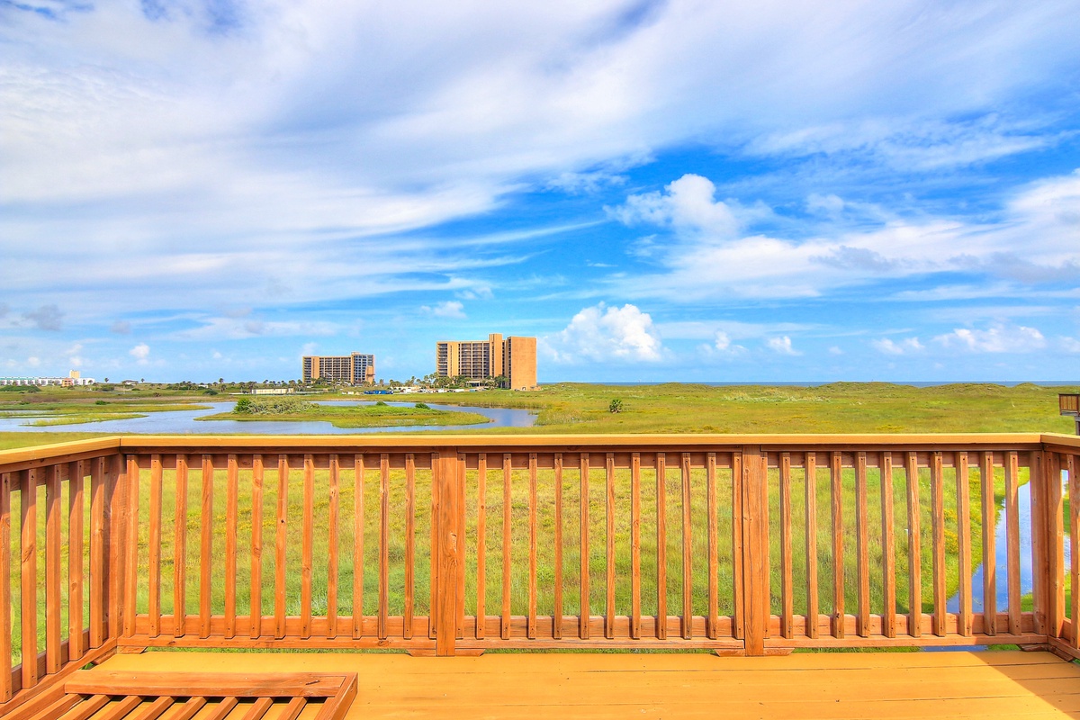 Expansive coastal view from private deck showcasing wetlands, distant buildings, and endless blue skies.