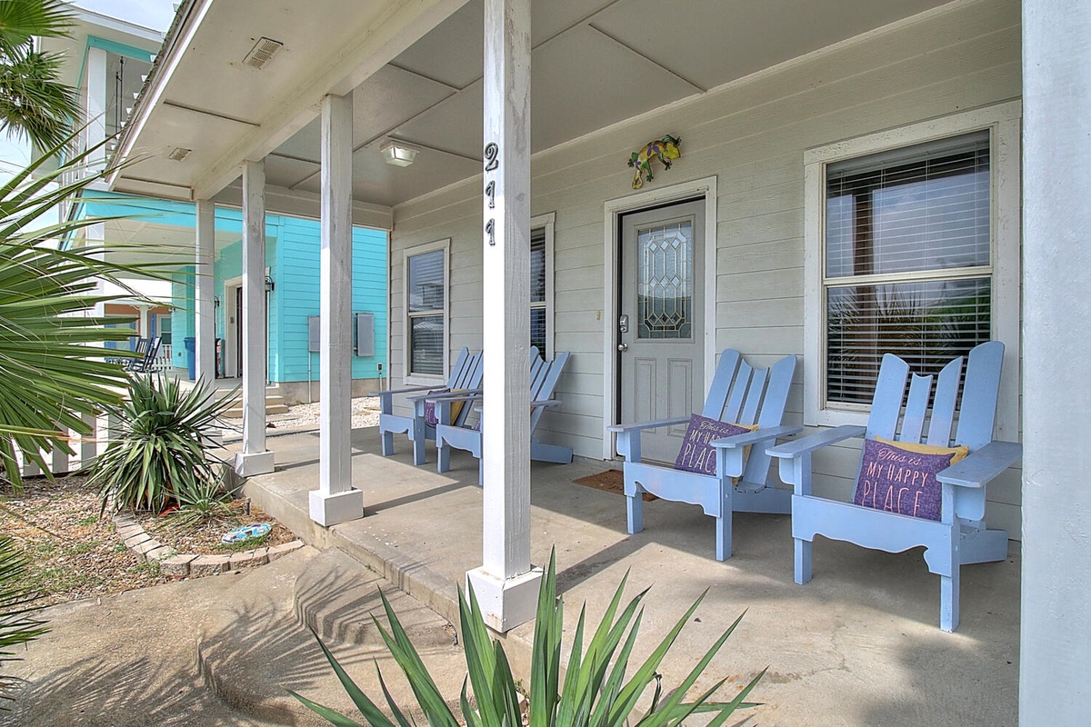 Your covered front porch welcomes you with cheerful blue Adirondack chairs, perfect for sipping morning coffee surrounded by tropical plants.