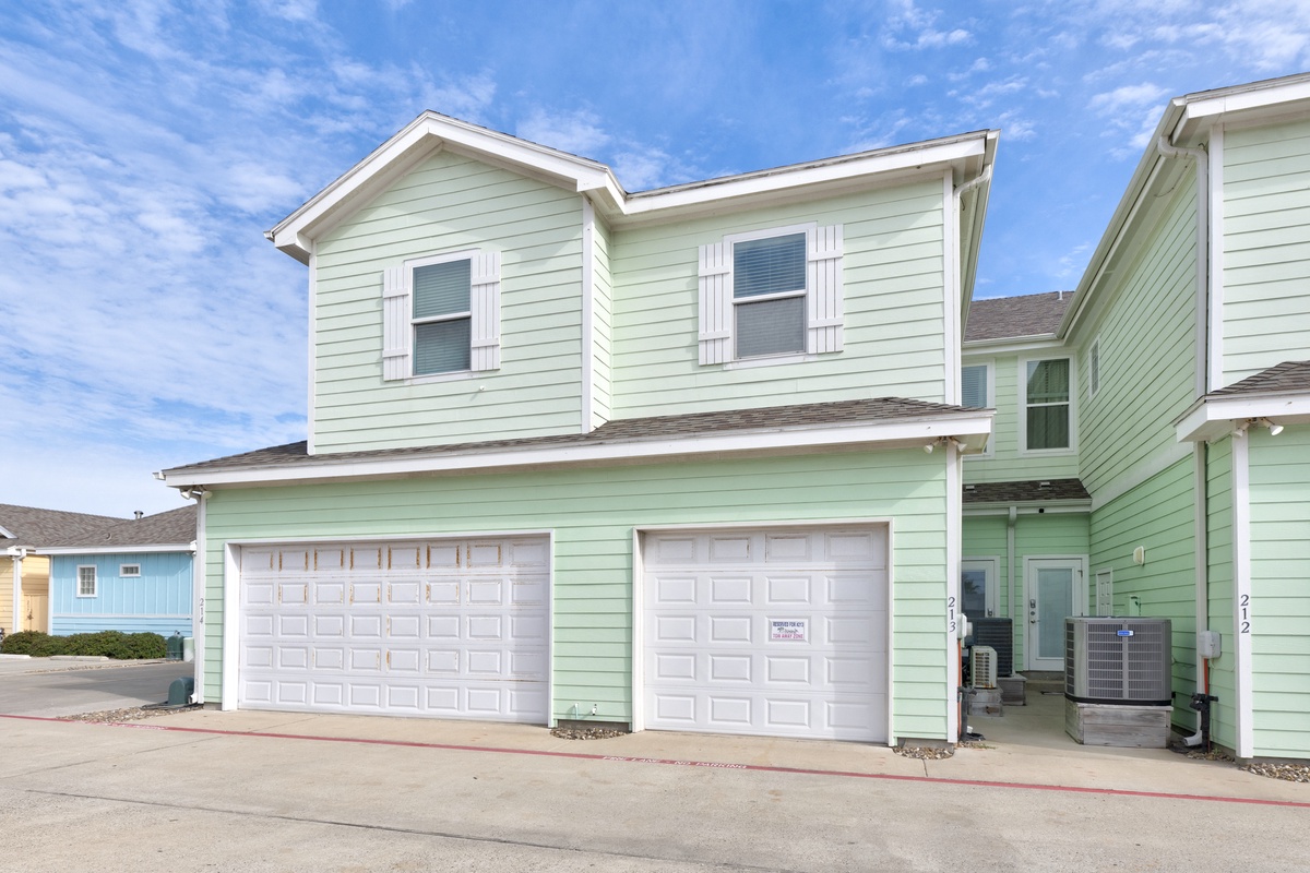 Charming green beach house exterior with convenient garage parking in a peaceful coastal neighborhood.