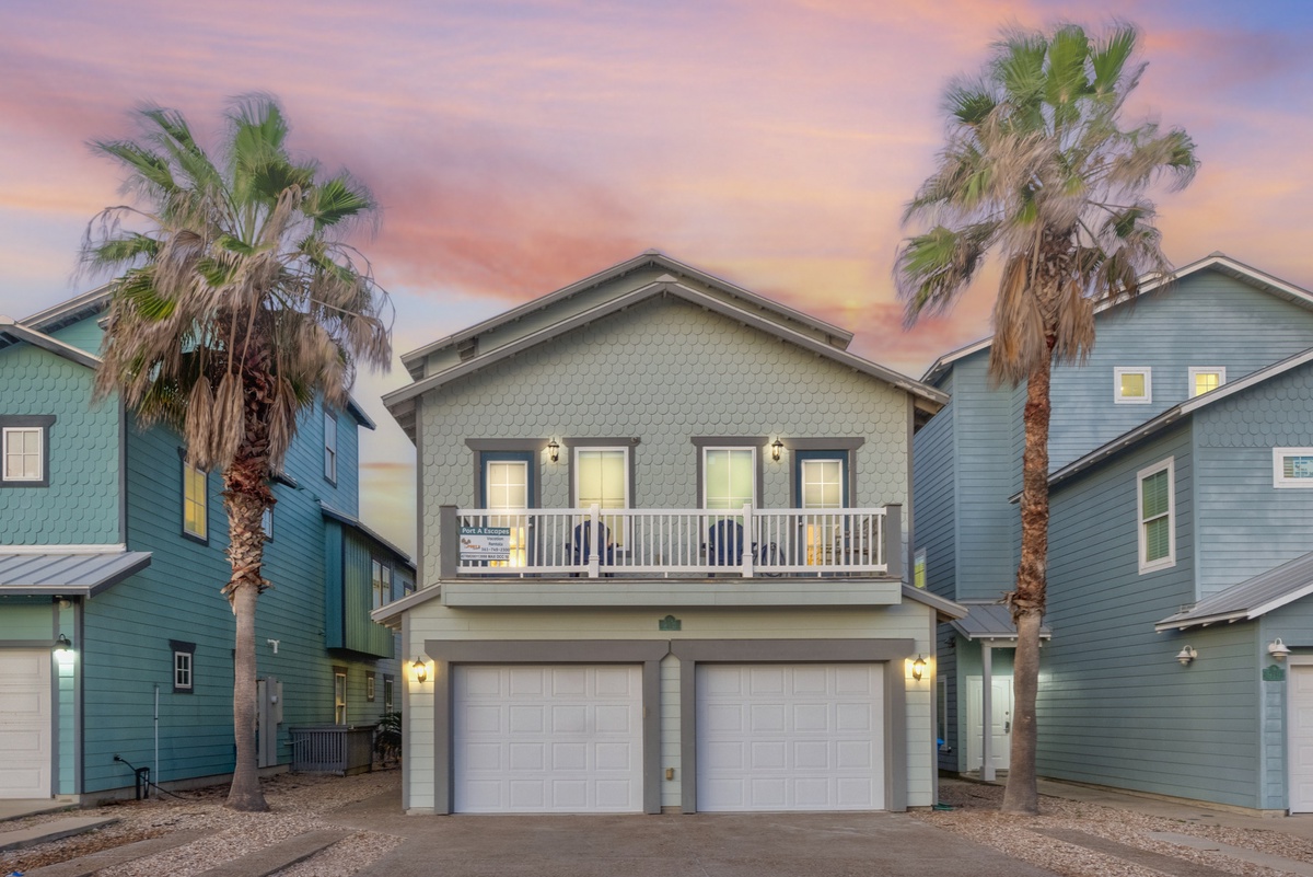 Modern coastal property with balcony and garage spaces nestled among palm trees, captured during a stunning sunset sky.
