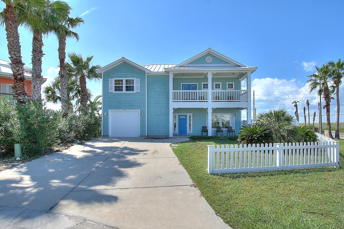 Charming turquoise beach house with white picket fence and swaying palms creates the perfect coastal retreat.