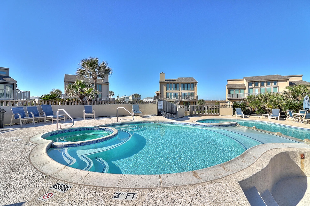 Sparkling pool area with hot tub under clear blue skies, surrounded by palm trees and beach homes.