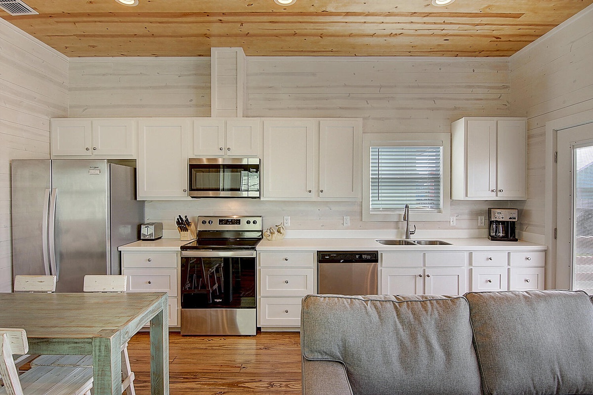 Relax in your open-concept retreat with a fully equipped kitchen featuring stainless appliances and cozy living space under rustic wood beams.